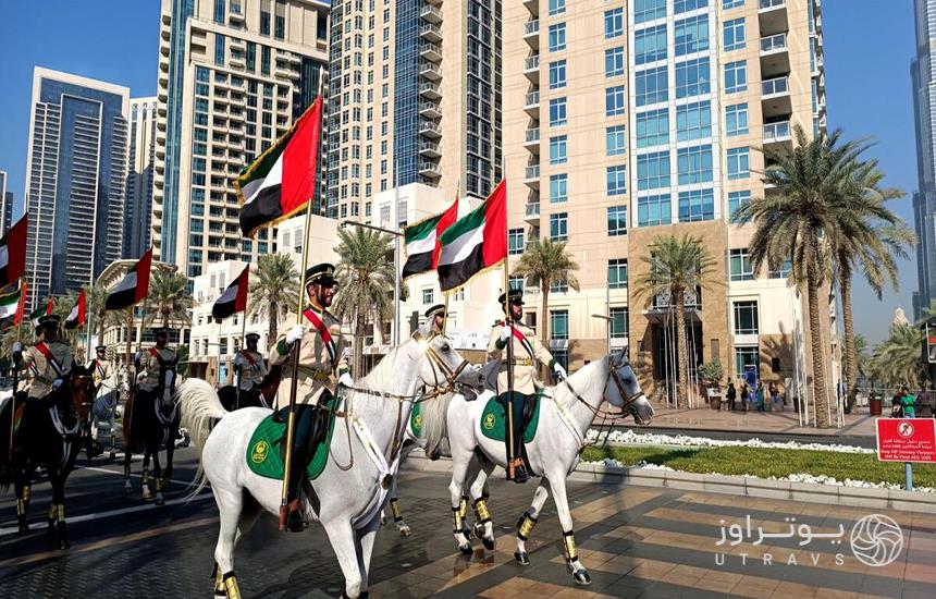 چند اسب‌سوار یونیفرم‌پوش که پرچم‌ امارات در دست دارند.